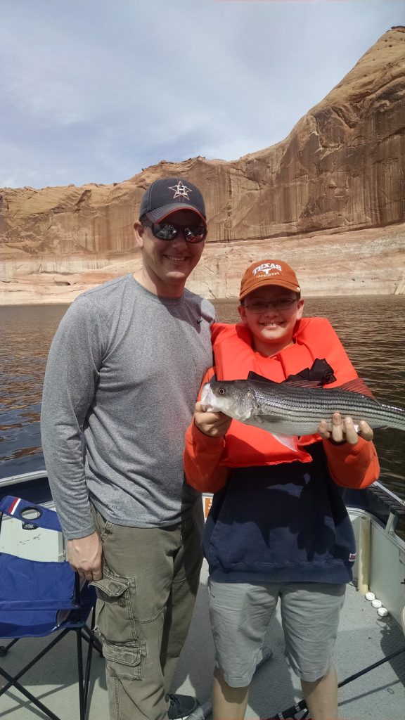 Image is of a father and his son holding their freshly caught fish while on a fishing trip at the lake.