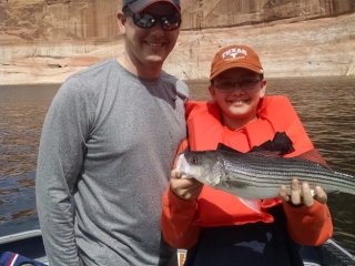 Image is of a father and his son holding their freshly caught fish while on a fishing trip at the lake.