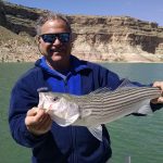 Image is of an angler holding his freshly caught fish on a sunny day on the lake.