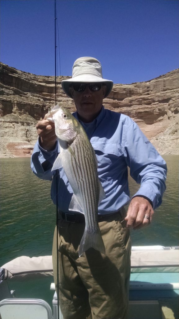 Image is of an angler holding his freshly caught fish while on a fishing trip at the lake.