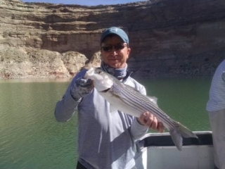 Image is of an angler holding his freshly caught fish while on a fishing trip at the lake.