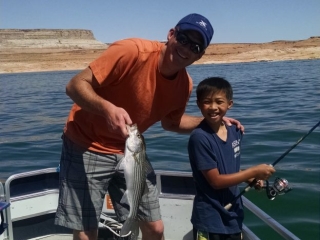 Image shows a young boy and a man holding a freshly caught fish on a sunny day, while fishing on the lake.
