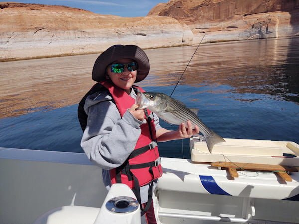 Young boy, early teen, on a boat smiling and holding up the fish he landed on Lake Powell