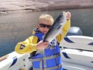 Young boy, pre-teen, on a boat smiling and holding up the fish he landed on Lake Powell