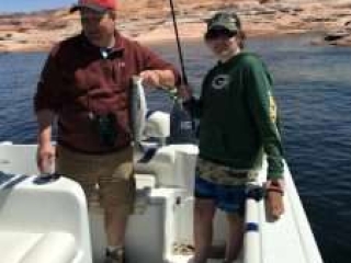 Virginia family enjoying fishing on Lake Powell - man and woman in a boat holding fishing rod and a landed stiper.