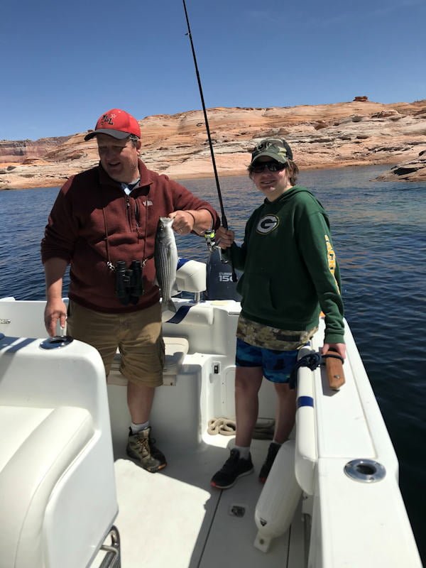 Virginia family enjoying fishing on Lake Powell - man and woman in a boat holding fishing rod and a landed stiper.