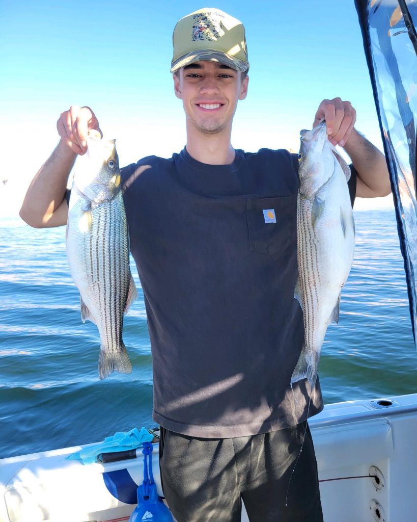 Young Man on a boat holding uup two fat Striped Bass he caught fishing with Capt Bill on Lake Powell, in Arizona.